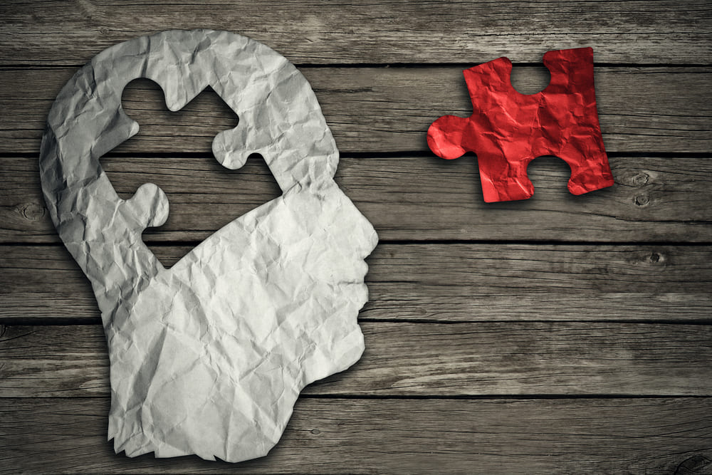 Puzzle head brain concept as a human face profile made from crumpled white paper with a jigsaw piece cut out on a rustic old wood background as a mental health symbol.