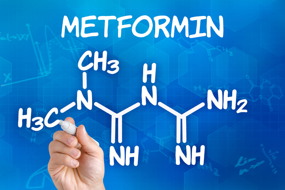 Hand with pen drawing the chemical formula of metformin