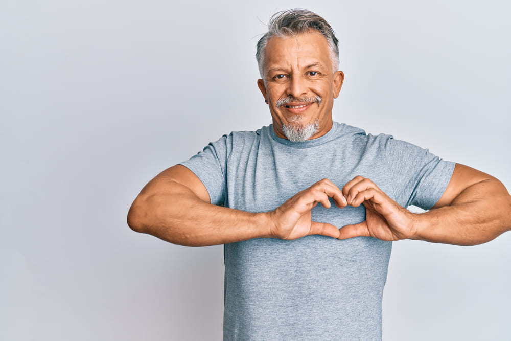 Middle age grey-haired man wearing casual clothes smiling in love doing heart symbol shape with hands.