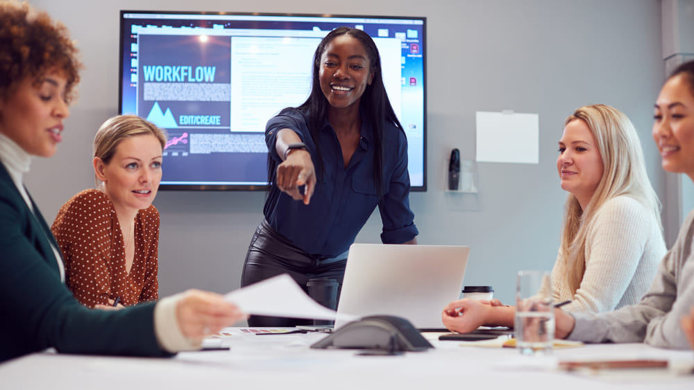 Young Businesswoman Leading Creative Meeting Of Women Collaborating Around Table In Modern Office